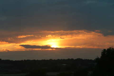Solnedgang ved Five Waterings-chalet i Storbritannien med mørke skyer og et varmt gyldent lys på himlen.