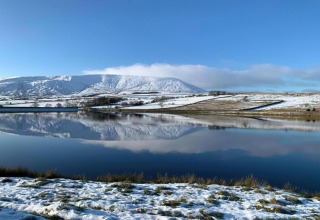 Snedækket landskab og bjerge spejler sig i en sø ved Five Waterings-chalet, Storbritannien, under klar himmel.
