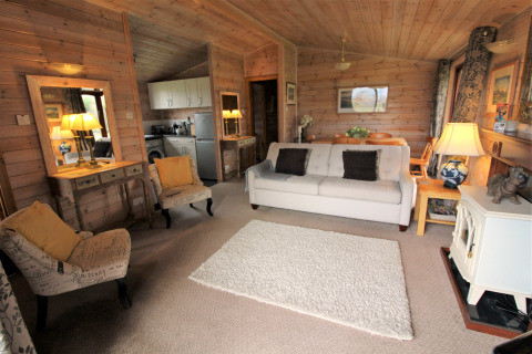 Acogedor salón de una cabaña de madera en Rainbow Petty, Reino Unido, con sofá, sillones y cocina abierta.