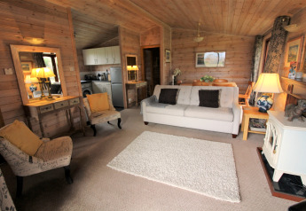 Acogedor salón de una cabaña de madera en Rainbow Petty, Reino Unido, con sofá, sillones y cocina abierta.
