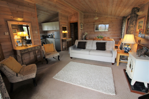 Accogliente soggiorno in legno della lodge Rainbow Petty nel Regno Unito con divano, poltrone e cucina aperta.