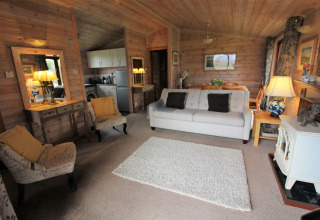 Accogliente soggiorno in legno della lodge Rainbow Petty nel Regno Unito con divano, poltrone e cucina aperta.