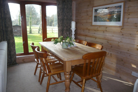 Sala da pranzo con tavolo in legno, sei sedie e ampie finestre con vista giardino al Rainbow Petty Lodge UK.
