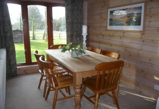 Sala da pranzo con tavolo in legno, sei sedie e ampie finestre con vista giardino al Rainbow Petty Lodge UK.