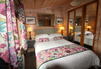 Dormitorio en una cabaña de madera con cama doble, armario con espejos y cortinas florales coloridas.