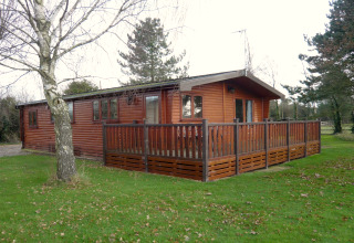 Cabaña Rainbow Petty en Reino Unido, construida en madera, con terraza vallada y rodeada de árboles y césped.