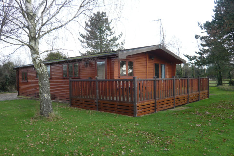 Lodge Rainbow Petty nel Regno Unito, una baita in legno con veranda recintata, immersa nel verde e alberi.