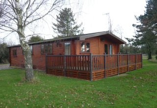 Lodge Rainbow Petty nel Regno Unito, una baita in legno con veranda recintata, immersa nel verde e alberi.