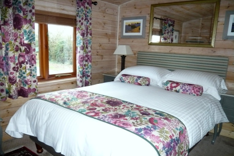 Camera da letto al Rainbow Petty Lodge, UK, con decoro floreale, pareti in legno e finestra luminosa.
