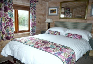 Camera da letto al Rainbow Petty Lodge, UK, con decoro floreale, pareti in legno e finestra luminosa.
