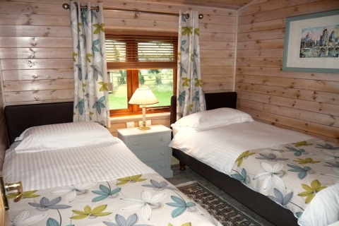 Dormitorio acogedor con dos camas individuales, decoración floral y vista al jardín en Rainbow Petty Lodge, Reino Unido.