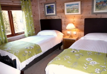 Habitación acogedora con dos camas individuales, cortinas verdes y paredes de madera en Rainbow Petty lodge.