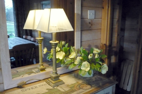 Lámpara y flores en una mesa junto a un espejo que refleja el interior acogedor de Rainbow Petty en el Reino Unido.