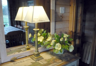 Lámpara y flores en una mesa junto a un espejo que refleja el interior acogedor de Rainbow Petty en el Reino Unido.