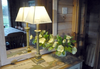 Lámpara y flores en una mesa junto a un espejo que refleja el interior acogedor de Rainbow Petty en el Reino Unido.