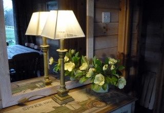 Lampada e fiori su un tavolo davanti a uno specchio, riflettendo l’interno della Rainbow Petty lodge nel Regno Unito.