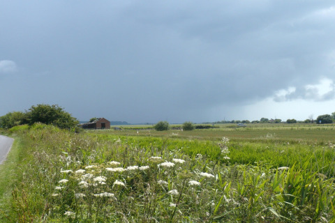 Vista di campi verdi e una strada di campagna vicino al lodge Rainbow Petty sotto un cielo nuvoloso nel Regno Unito.