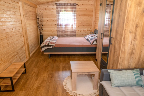 Knusse houten bungalow met tweepersoonsbed, bank en tafel bij Robinzonski Kamp Hofman in Kroatië.