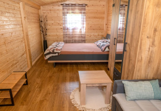 Knusse houten bungalow met tweepersoonsbed, bank en tafel bij Robinzonski Kamp Hofman in Kroatië.