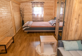 Cozy wooden bungalow with double bed, sofa, and table at Robinzonski Kamp Hofman, Croatia.