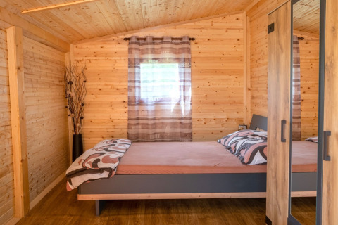 Slaapkamer in een stacaravan met houten wanden, tweepersoonsbed en kast bij Robinzonski Kamp Hofman, Kroatië.