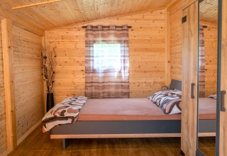 Slaapkamer in een stacaravan met houten wanden, tweepersoonsbed en kast bij Robinzonski Kamp Hofman, Kroatië.