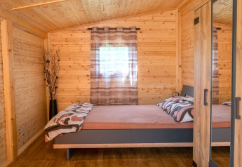 Camera da letto in una casa mobile con pareti in legno, letto matrimoniale e armadio a Robinzonski Kamp Hofman, Croazia.