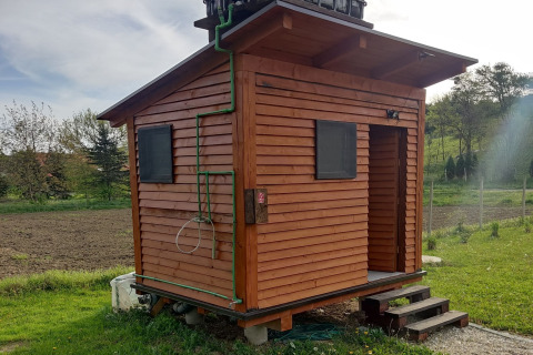 Kleine houten mobiele woning bij Robinzonski Kamp Hofman in Kroatië met groene leidingen en platteland.