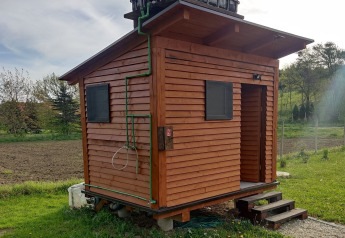 Piccola casa mobile in legno al Robinzonski Kamp Hofman, Croazia, con tubi verdi e paesaggio rurale.