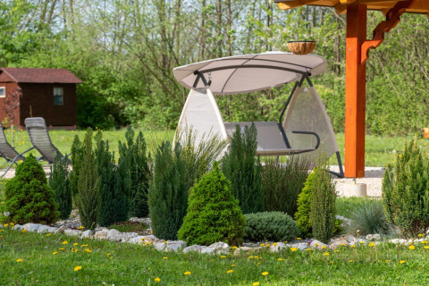 Tuin met groenblijvende struiken, schommelstoel en prieel bij Robinzonski Kamp Hofman - Private Bungalow, Kroatië.