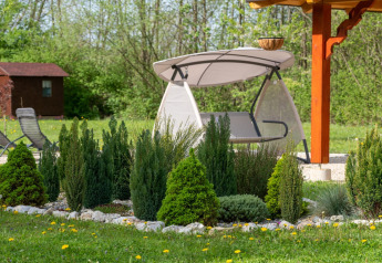 Giardino con arbusti sempreverdi, dondolo e gazebo presso Robinzonski Kamp Hofman - Bungalow Privato, Croazia.