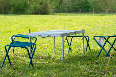 Opvouwbare tafel met vier campingkrukjes op het gras bij Robinzonski Kamp Hofman in Kroatië.