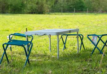 Outdoor setting with a folding table and four camping stools on grass at Robinzonski Kamp Hofman in Croatia.