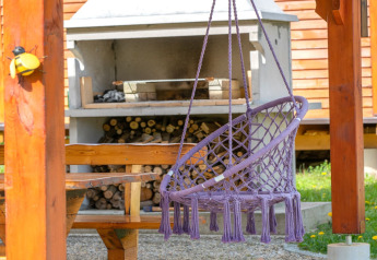 Outdoor purple hanging chair, wooden table, and fireplace at Robinzonski Kamp Hofman, Croatia.