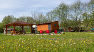 Mobiele bungalow in Robinzonski Kamp Hofman met terrasoverkapping, bloemenveld en bos op de achtergrond.