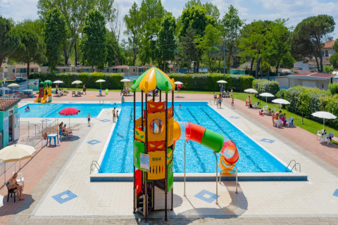 Außenpool mit Rutsche und Liegestühlen beim Mobilheim Cottage «Cesenatico» in Italien an einem sonnigen Tag.