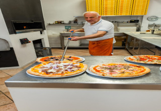 Ein Pizzabäcker bereitet frische Pizzen in einer modernen Küche im Mobilheim Cottage „Cesenatico“ in Italien zu.