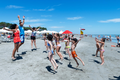 Kinder und Erwachsene springen und spielen am Strand beim Mobilheim Cottage Cesenatico in Italien.