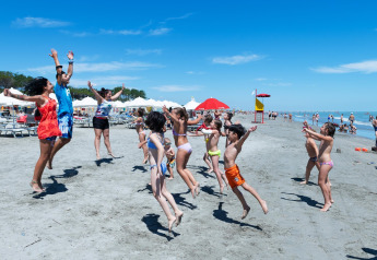 Børn og voksne hopper og leger på stranden ved mobilhome Cottage Cesenatico i Italien, med sol og blå himmel.