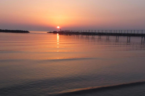 Zonsondergang boven kalm water gezien vanuit een stacaravan, met een lange pier en zachte kleuren.