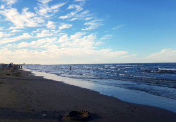 Rustig strand met zachte golven, blauwe lucht en mensen bij een stacaravanterrein aan zee.