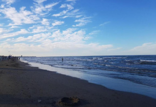 Ein ruhiger Strand mit sanften Wellen, blauem Himmel und Menschen, nahe einem Mobilheim-Gebiet am Meer.