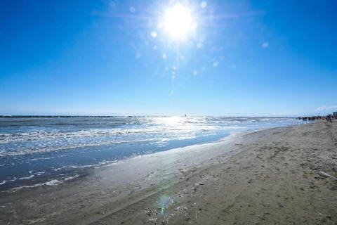 Zonnige stranddag met blauwe lucht en rustige golven, gefotografeerd vanaf een stacaravan aan zee.