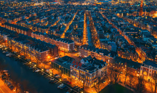Vista aérea nocturna de una ciudad con canales y alojamientos glamping en un parque vacacional iluminado.