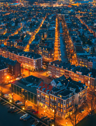 Vista aérea nocturna de una ciudad con canales y alojamientos glamping en un parque vacacional iluminado.