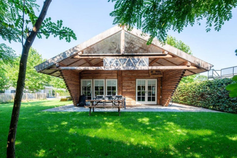 Paalchalet 723 i Belgien, et træhytte-lodge med store glasdøre omgivet af frodig grøn have og træer.