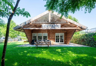 Paalchalet 723 i Belgien, et træhytte-lodge med store glasdøre omgivet af frodig grøn have og træer.