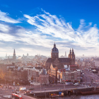 Vista panorámica de Ámsterdam central con edificios históricos, canales y cielo azul en un día soleado.