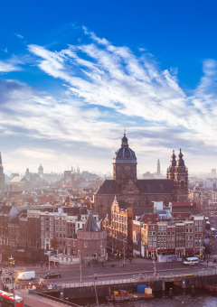 Vista panorámica de Ámsterdam central con edificios históricos, canales y cielo azul en un día soleado.