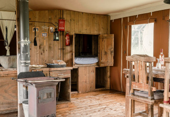 Rustic lodge interior with wooden furniture, a stove, and large window at Duynlodge - Duynpark, Netherlands.